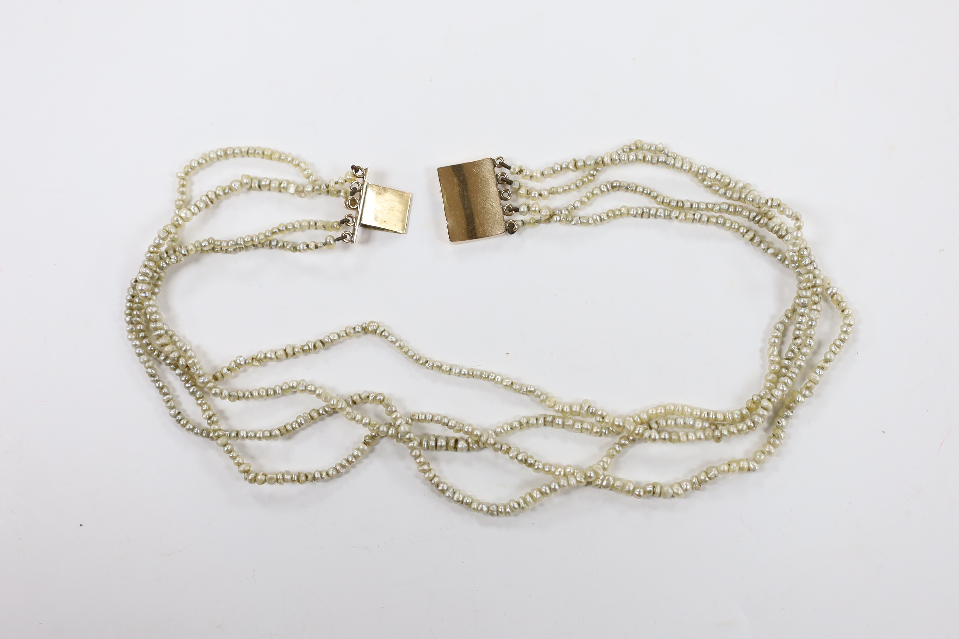 A Regency four (ex five) strand seed pearl choker necklace, with rectangular engraved yellow metal clasp, 37cm.